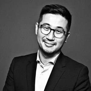 Black and white head shot of Paul Cheung, an Asian-American man wearing a dark jacket and glasses