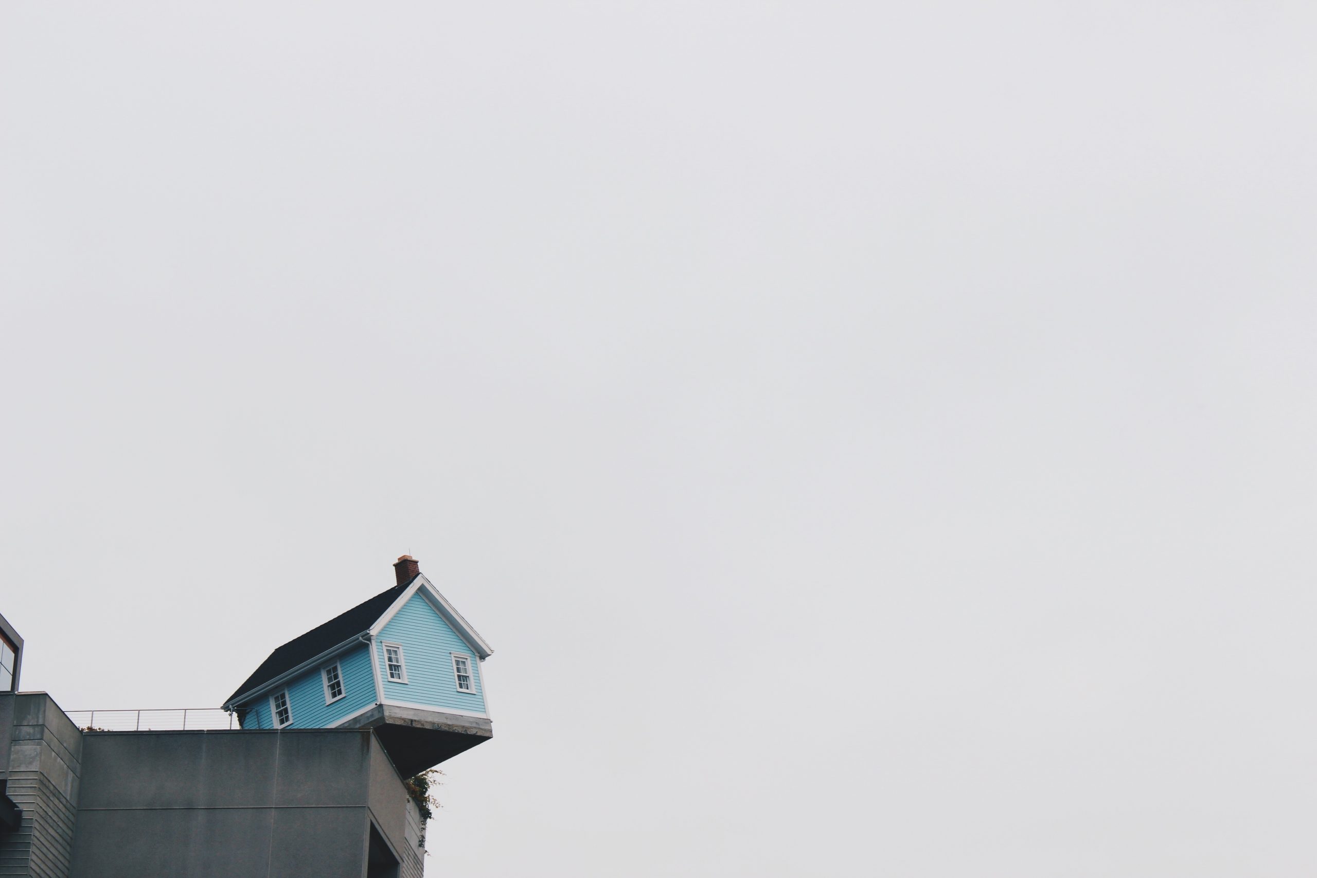 Photo of a teal house sitting out on the edge of a cliff.