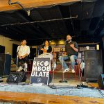 Photo of three people on a panel with a "Recombulate" poster in the foreground.