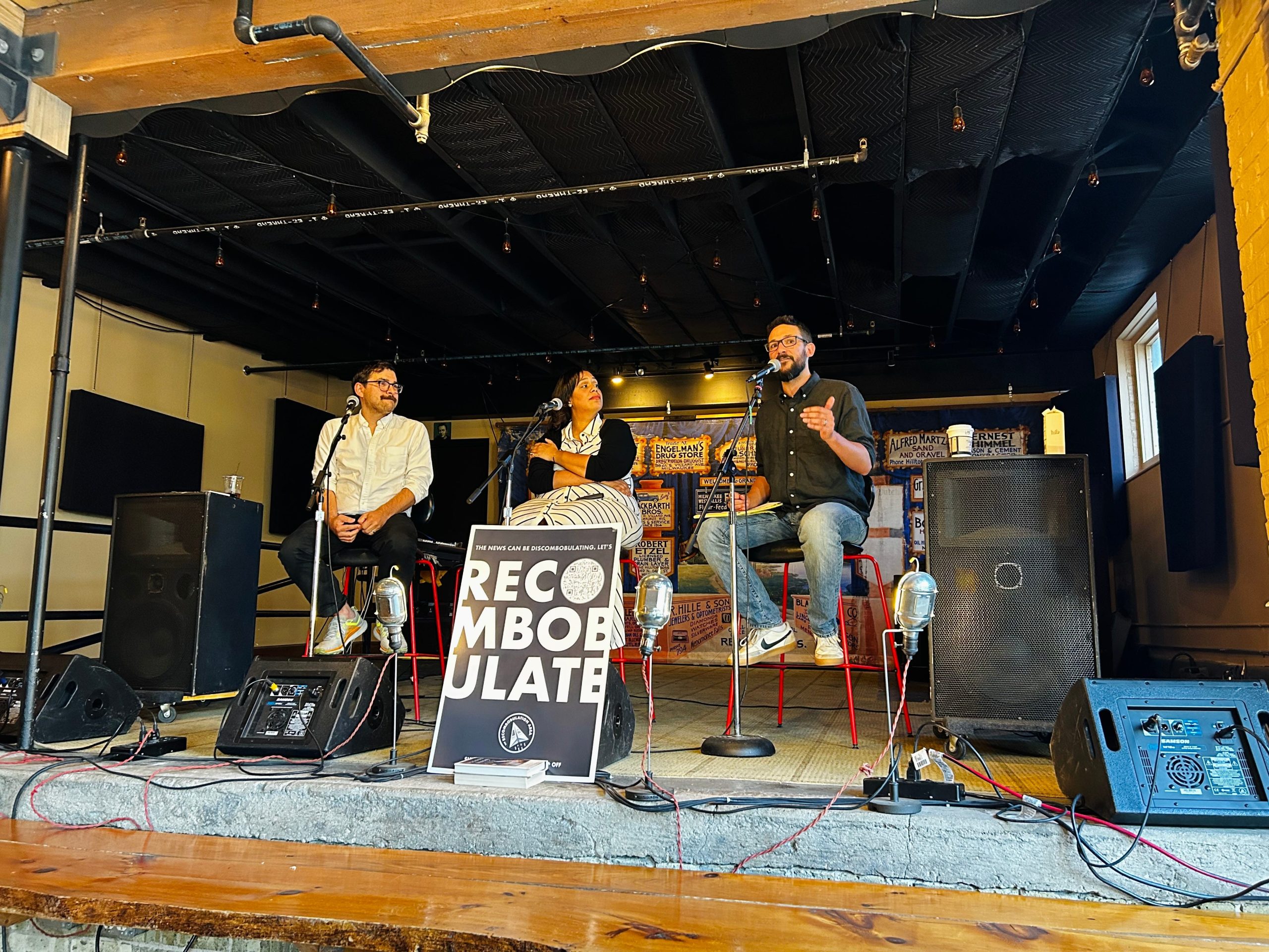Photo of three people on a panel with a "Recombulate" poster in the foreground.