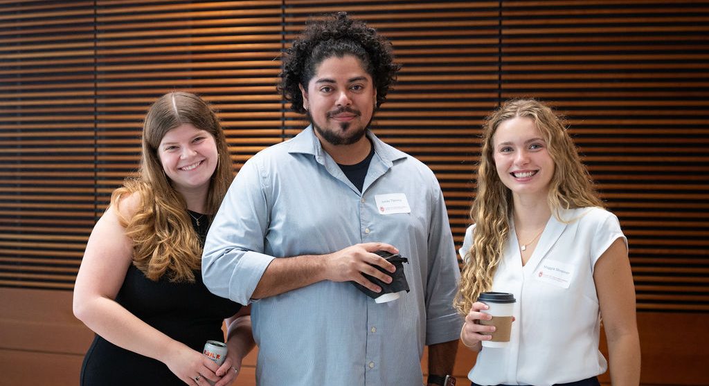 Three fellows pose for a photo at the registration table of the 2025 ethics conference.