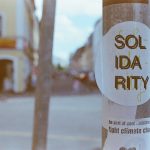 Photo of city street with a "Solidarity" sticker shown on a pole in the foreground