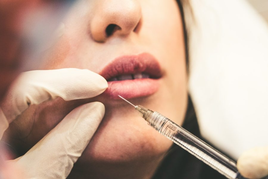 Photo of woman's face from nose down, with a filler needle approaching her lips.