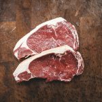 Image of two uncooked steaks laid on a wooden cutting board.