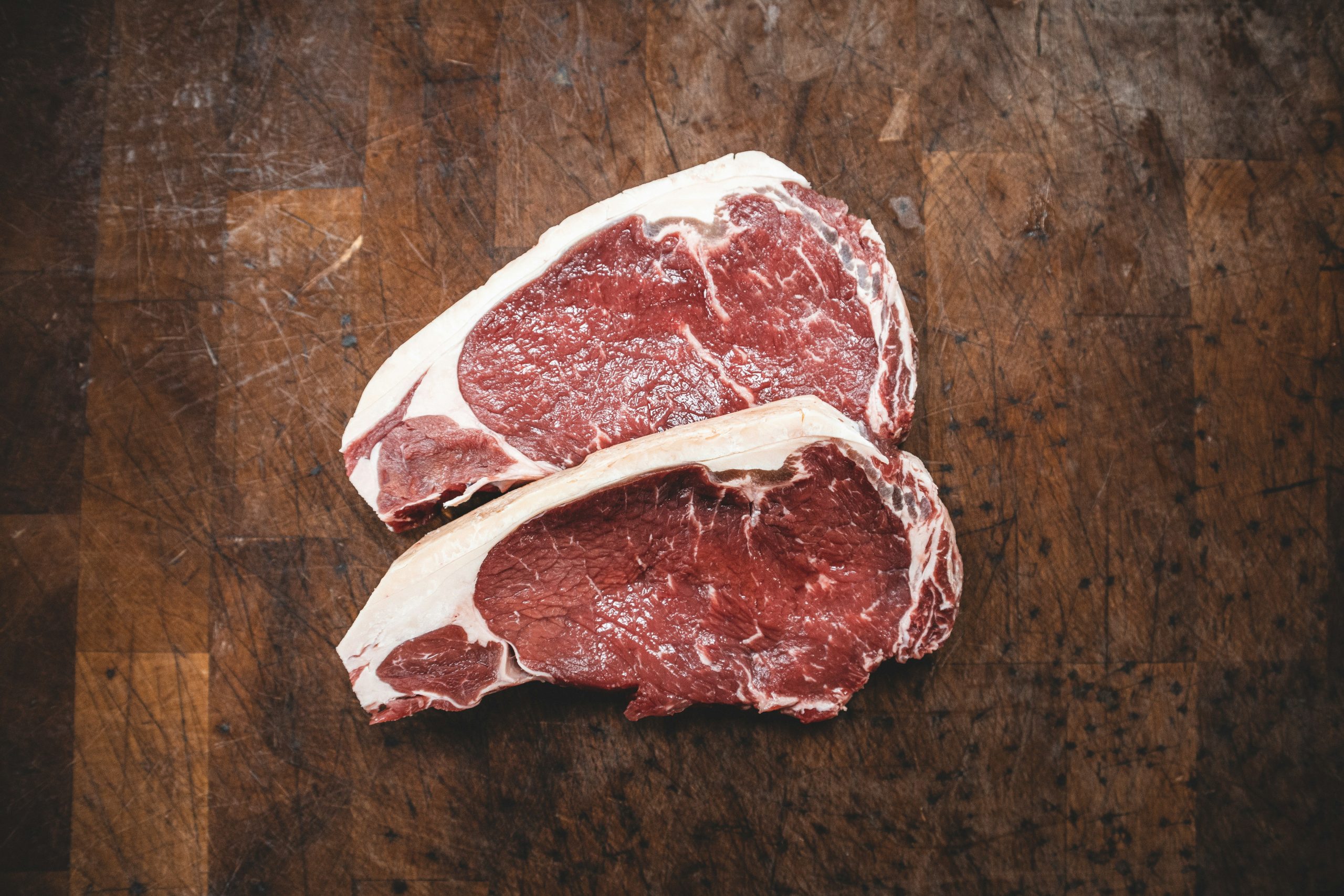 Image of two uncooked steaks laid on a wooden cutting board.
